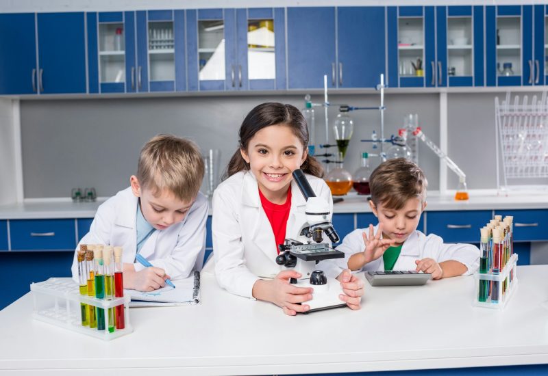 three-kids-in-chemical-laboratory-making-notes-and-using-microscope-and-calculator-1.jpg